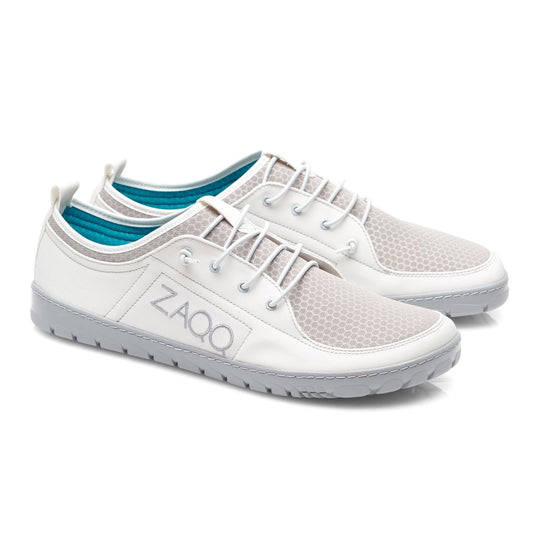 Ein Paar stylische SQY-White-Sneaker von ZAQQ besteht aus strukturiertem Stoff in einem cremefarbenen Farbton auf der Oberseite, ergänzt durch graue Sohlen. Der Markenname ZAQQ ist auf der Seite sichtbar. Das türkisfarbene Innenfutter sorgt für einen lebendigen Kontrast. Diese Schuhe werden nebeneinander platziert, um ein elegantes Aussehen zu erzielen.