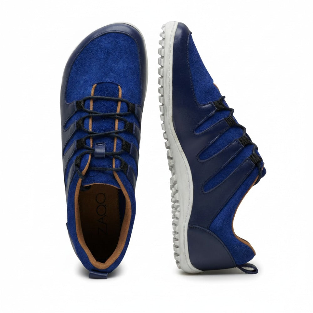 Ein Paar stylische blaue und dunkelblaue SHOQQ Trident-Sneaker von ZAQQ mit weißen Kautschuksohlen. Ein Schuh steht aufrecht, während der andere auf der Seite liegt und das strukturierte Sohlenmuster und das geschnürte Obermaterial aus Nappaleder zur Geltung bringt.