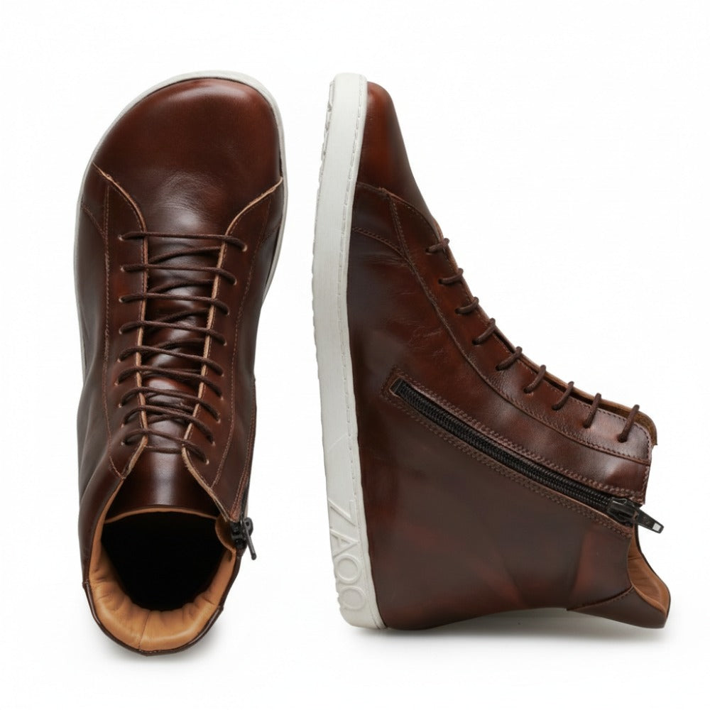 Ein Paar SNAQ Antique Brown High-Top-Sneaker aus Nappaleder mit weißer Sohle. Ein Schuh steht aufrecht und zeigt Schnürsenkel und Zehenpartie, während der andere auf der Seite liegt und einen seitlichen Reißverschluss und den Markennamen ZAQQ an der Ferse aufweist.